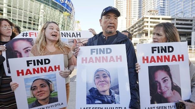 Two women flank a man wearing a baseball cap. They are all standing outside an area, holding signs with an image of another woman. The signs say, 'Find Hannah.'