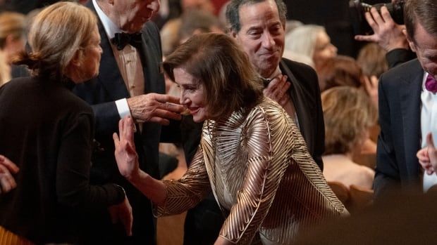 An older woman shakes hands with someone in a  room full of people in gala clothing