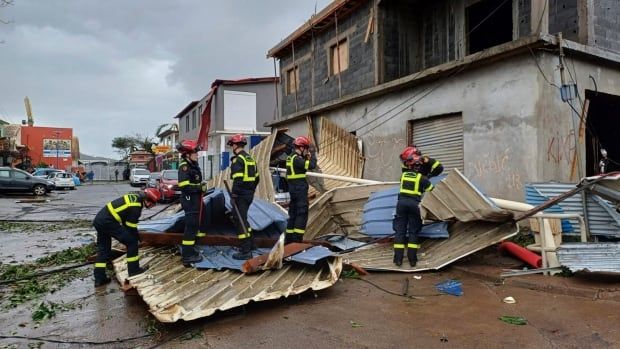 Rescue workers clear debris on a road next to a heavily damaged building.