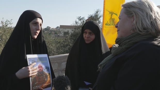 Two women face eachother one holds up photo of a man