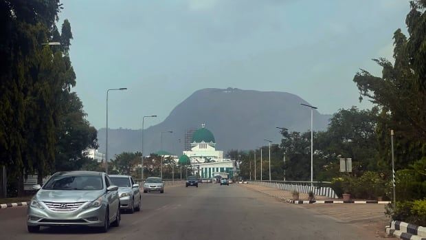 Cars drive on a road as a large building is seen in the background.