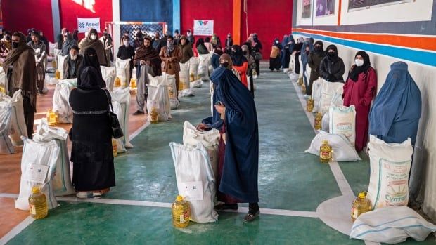 People stand next to bags of food aid inside a gymnasium.