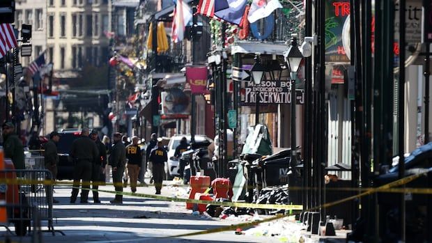 People wearing jackets with the letters FBI stand on a street with police tape and debris on the ground.