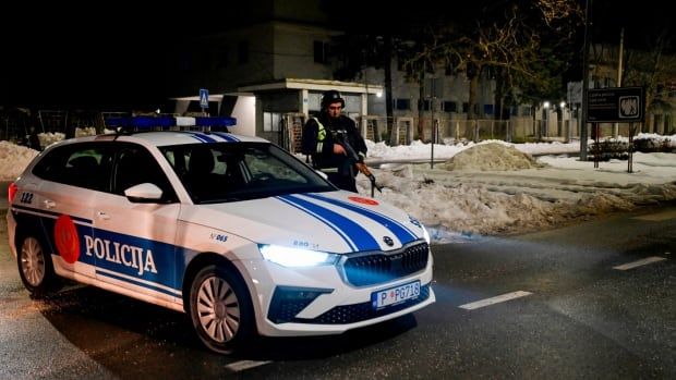 Armed officers stand guard around a police car.