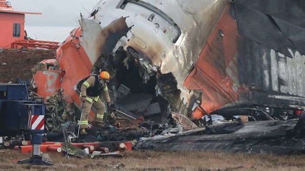 A firefighter in a hard hat sifts through the wreckage of a passenger jet that crashed.