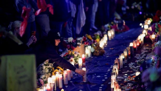 A mourner places a candle at a vigil.