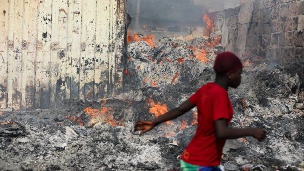 A young person in a red shirt walks past smouldering debris