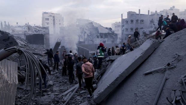 People navigate rubble after a building collapse in an urban area. Debris fills the scene, and smoke rises