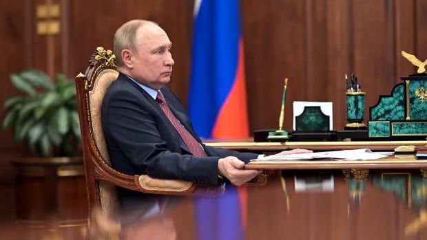 A man sits at a desk with the Russian flag in the background.