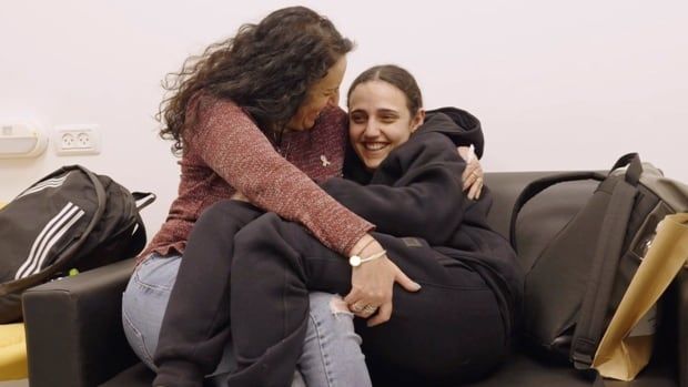 Two people smile while embracing on a couch.