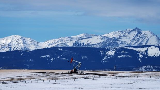 An oil pump jack is seen in front of a mountain range background.