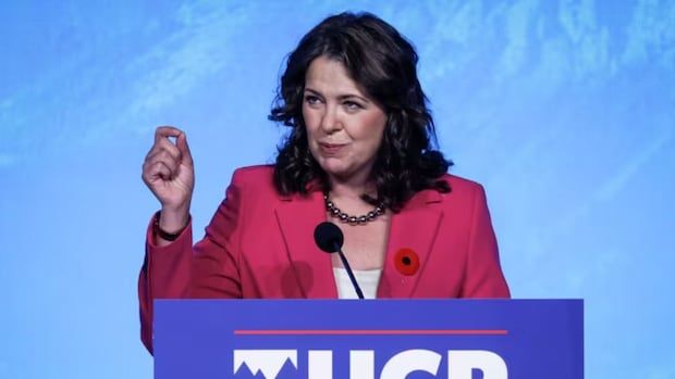 Danielle Smith, leader of Alberta's UCP, speaks into a microphone at a podium. 