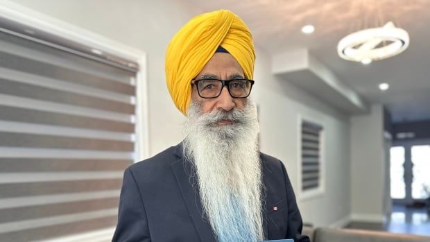 A Sikh man in a suit holding a passport 