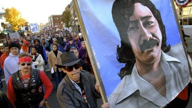 Ralliers march in the streets, some holding a large painting of Leonard Peltier.