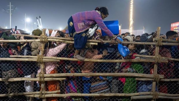 A person climbs over a fence with a large crowd behind the fence.