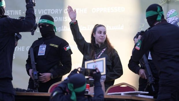 A young woman holds a plaque and waves stage. Beside her are two masked men wearing green headbands.