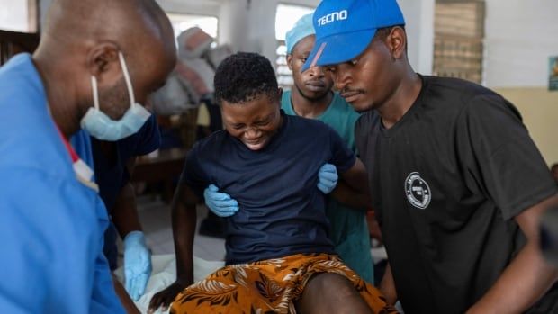 An injured person on a table grimaces as hospital workers tend to their wounds.