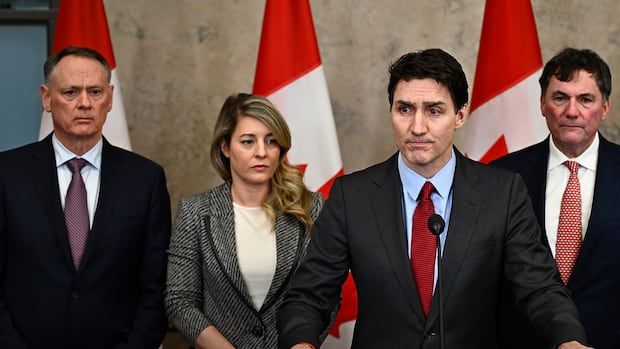 A man speaks into a microphone with three people standing behind him. 