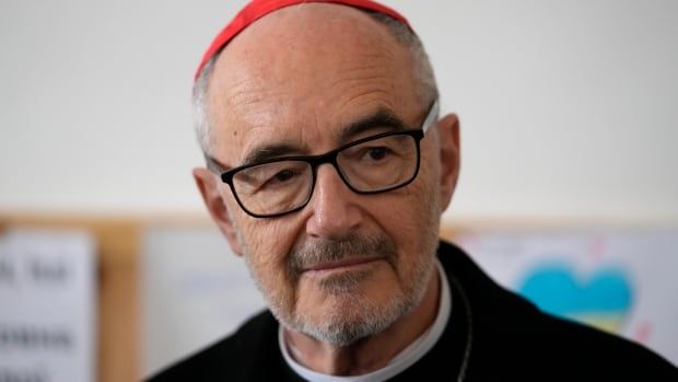 An older man with a salt and pepper beard wearing glasses is shown in closeup wearing religious garments and hat.