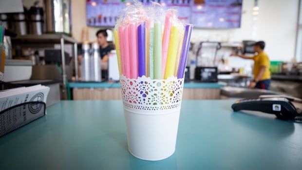 A small bucket of individually wrapped plastic straws sits on a cafe counter.