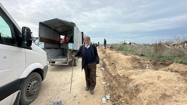 A man stands on the street with a walking stick