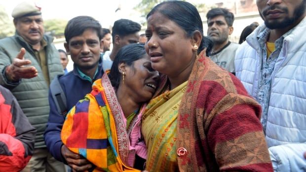 Two women stay close to each other and cry as men in the background look at them.