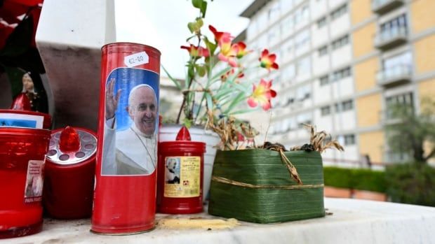 A candle with a picture of Pope Francis is set at the bottom of a statue. 