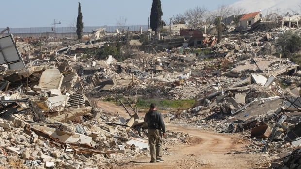 A man walks near damaged buildings.