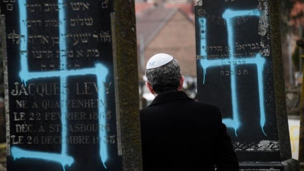 A man wearing a Kippah walks by graves vandalised with swastikas at the Jewish cemetery