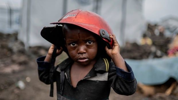 A young Congolese boy holds a broken helmet over his head.