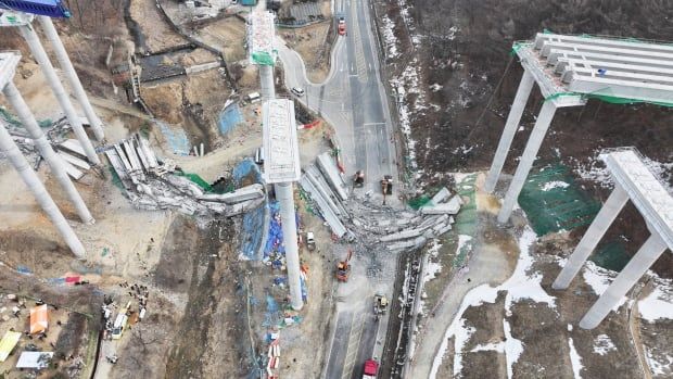 From an aerial view, a bridge that has crumbled in the middle is shown. Concrete debris are shown on the ground.