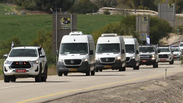 A convoy of white vans, about a half dozen, is shown on a road that appears to be in a rural setting.