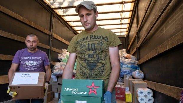 Two men unload boxes of various items from the back of a large truck. 