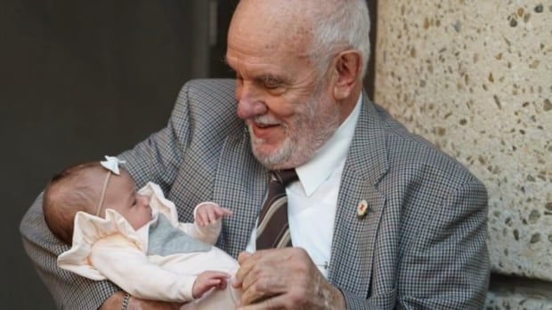 An older man in a suit holds a baby