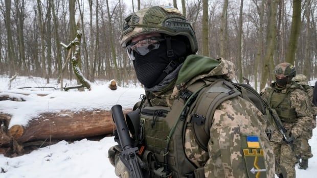 Soldiers, heavily bundled in camoflage winter gear, move through a snowy forest.