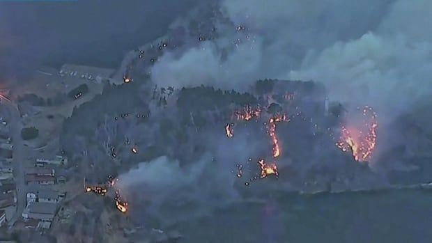 An aerial view of a Japanese city and a mountainous landscape with scattered pockets of fire.