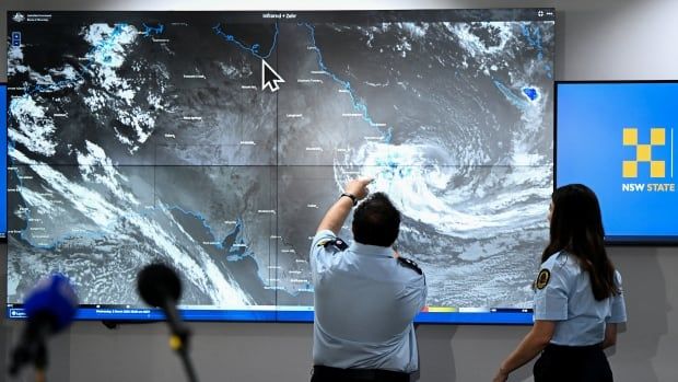 Two people gesture at a large screen showing a cyclone formation