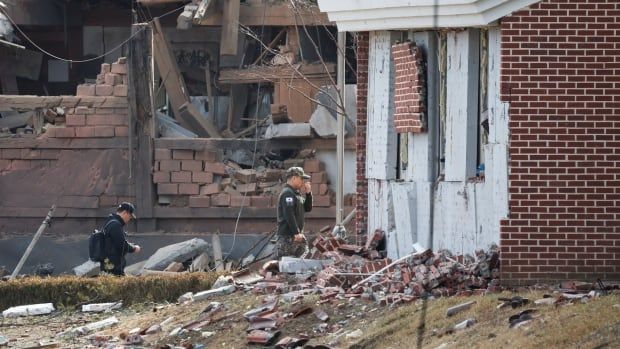 Officials in black clothes inspect damaged buildings, standing amidst brick and building rubble