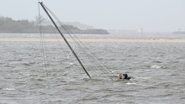 Two divers' heads are seen above choppy water next to the top of a submerged yacht