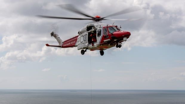 A helicopter hovers above water at what looks like the ocean. 