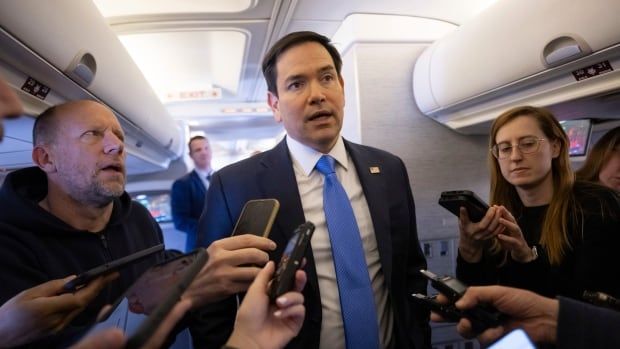 Journalists hold microphones to hear a man speak on a plane.