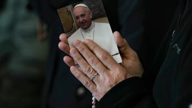 Praying hands hold a photo of Pope Francis.