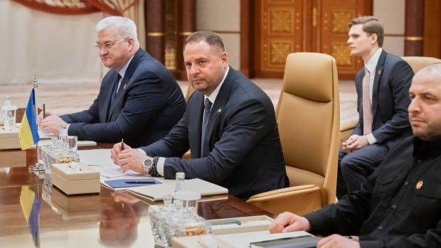 Three men sit at a conference table.