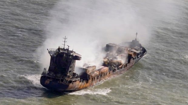 A smouldering cargo ship drifts in open water.