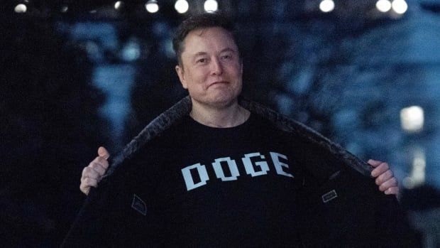 Elon Musk flashes his t-shirt that reads "DOGE" to the media as he walks on South Lawn of the White House, in Washington, Sunday, March 9, 2025. (AP Photo/Jose Luis Magana)