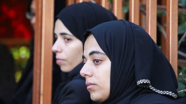 Palestinian women in hijabs sit next to one another. 