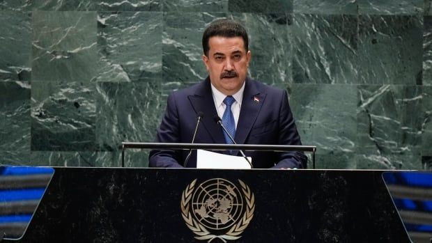 A man with a mustache wearing a suit stands behind a dais at the United Nations