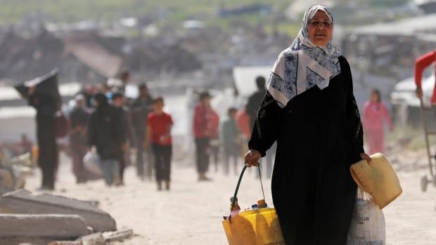 A woman carries belongings as she walks along a dirt road.