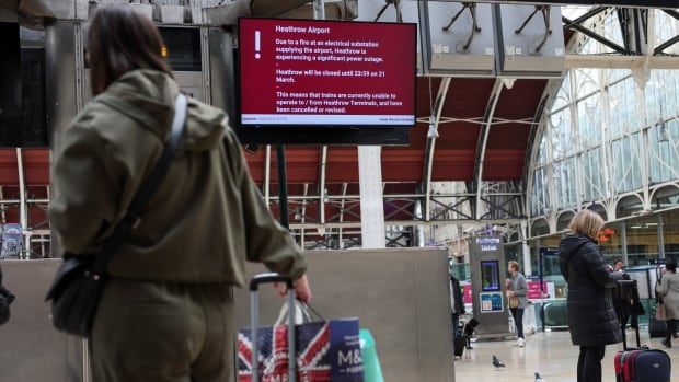 People stand with their backs to the camera carrying and guiding luggage, while looking toward an electronic bulletin board that says Heathrow Airport is closed.