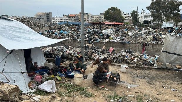 Children sit next to one another around a fire next to piles of garbage.